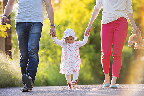 Parents holding daughters hand walking.